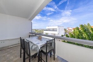 Ein Balkon mit Tisch und Stühlen, einem weißen Geländer und Blick auf Gebäude und Grünflächen.
