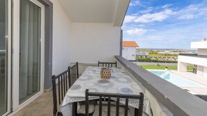 A balcony with a table and chairs, a view of a swimming pool, and a building in the background. - Apartment Perinic No.1 in Vrsi (Vrsi)
