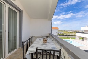 Ein Balkon mit Tisch und Stühlen, Blick auf einen Pool und ein Gebäude im Hintergrund.