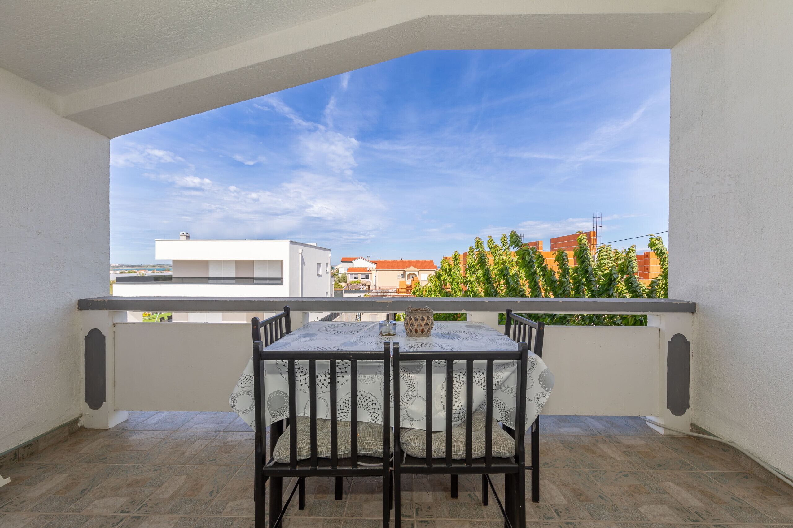 A balcony with a table and chairs, a view of buildings, and a clear sky.