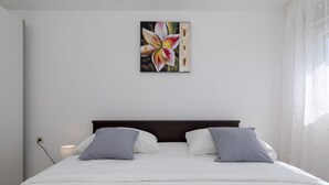 Een slaapkamer met een bed, kussens, een nachtkastje, een lamp en een aan de muur hangend schilderij.