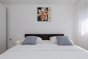 Ein Schlafzimmer mit Bett, Kissen, einem Nachttisch, einer Lampe und einem Wandbild.