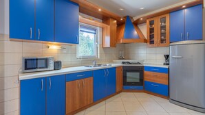 Een moderne keuken met blauwe kastjes, een magnetron, fornuis, spoelbak en koelkast.
