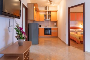 A compact kitchen with modern appliances, a dining area with a table and vase, and a bedroom with a bed and nightstand. - Holiday Home Maria with Private Beach Access (Vir)