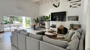 Ein modernes Wohnzimmer mit einem grauen Ecksofa, einem runden Couchtisch, einem flachbildfernseher an der Wand, einem Kamin und einem Essbereich mit Tisch und Stühlen.