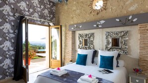 A hotel room with a bed, two decorative mirrors, a clock, and a view of a pool and garden. - Maison de la Combe charming barn with pool and valley views (Laparade)