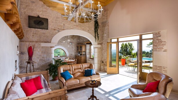 A spacious living area with a leather sofa, wooden furniture, and a large window offering a view of the outdoors. - Maison de la Combe charming barn with pool and valley views (Laparade)