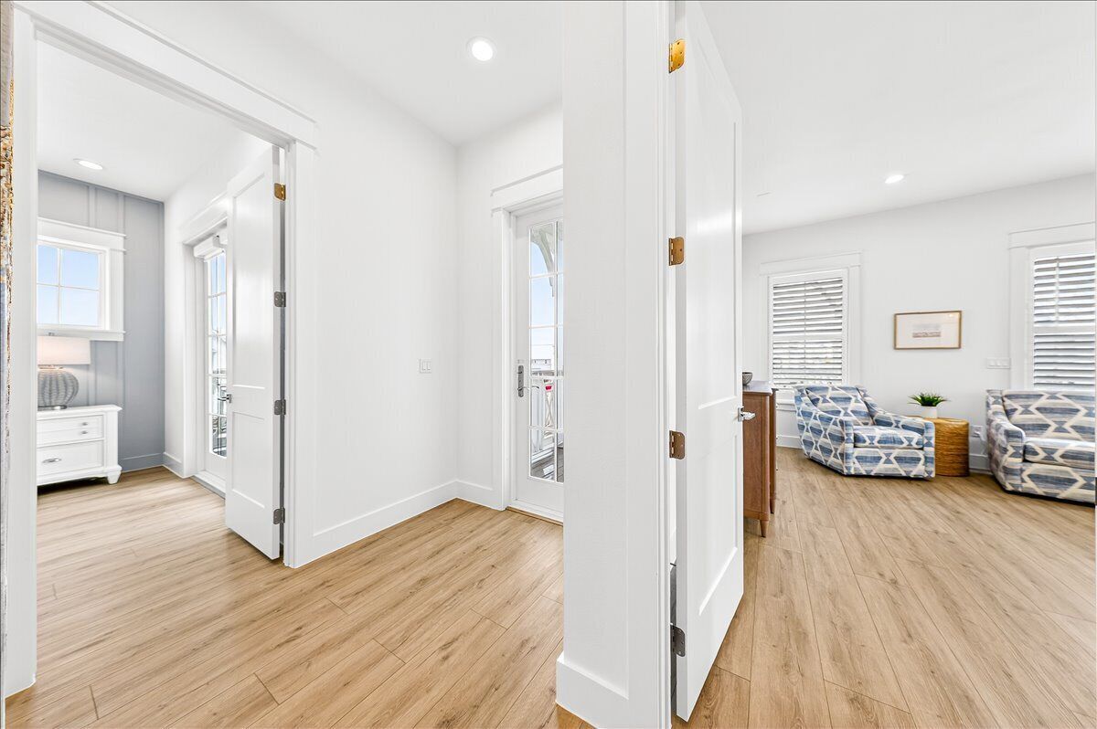 Een kamer met een houten vloer, witte muren, een witte deur, een witte dressoir en een bank met een patroon, plus een raam met jaloezieën.