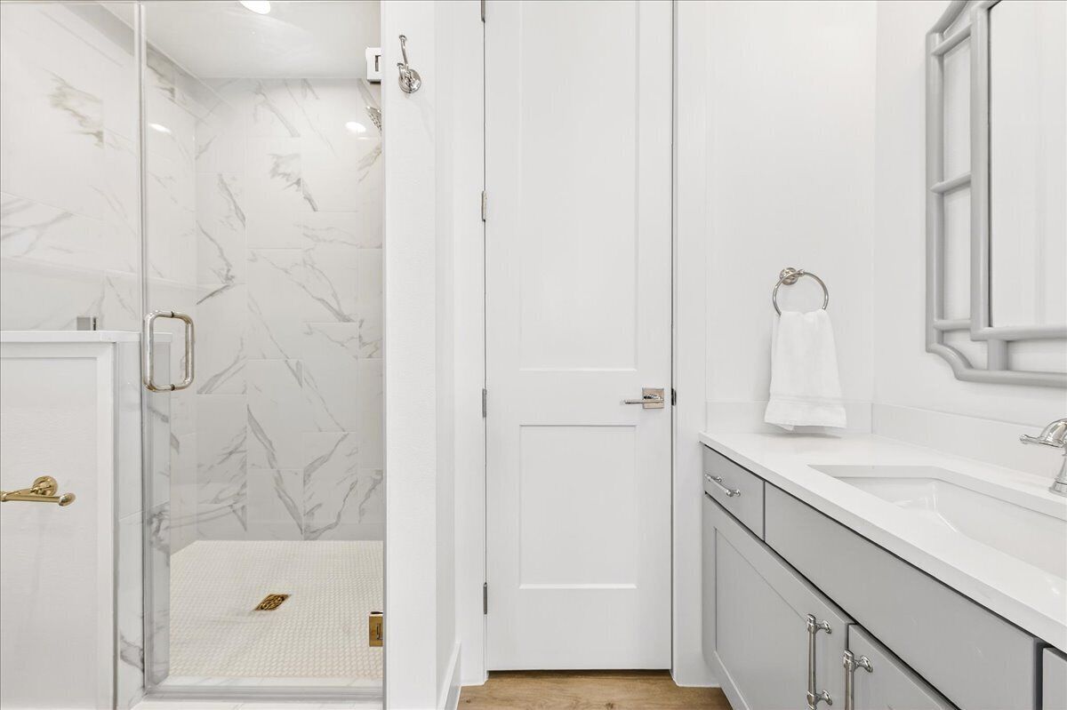 A modern bathroom with a glass shower enclosure, a white door, and a sink with a towel rack.