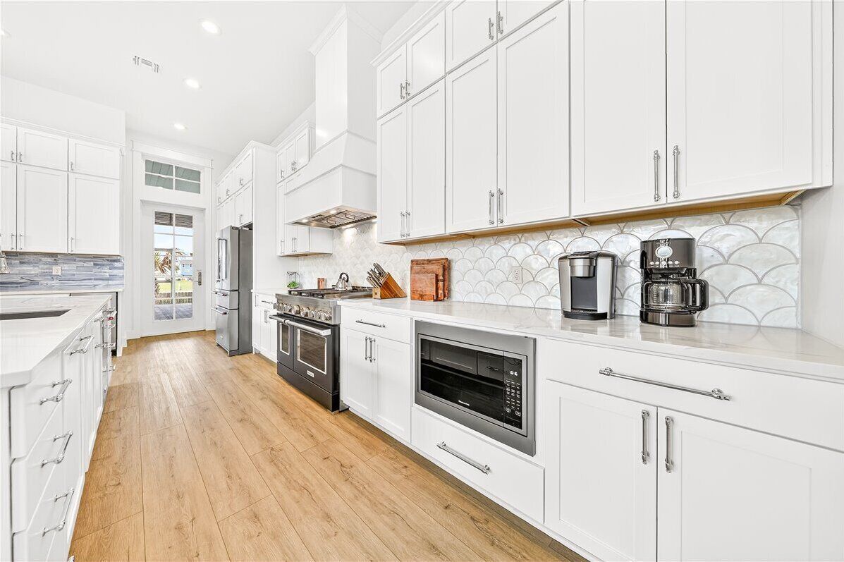 A modern kitchen with white cabinets, stainless steel appliances, and a wooden floor.