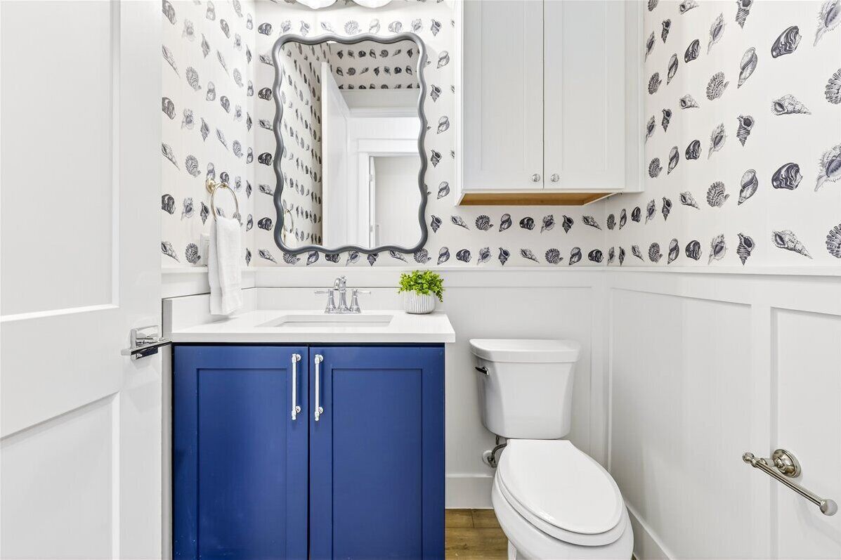 A bathroom with a white toilet, blue cabinets, a white sink, and a mirror.