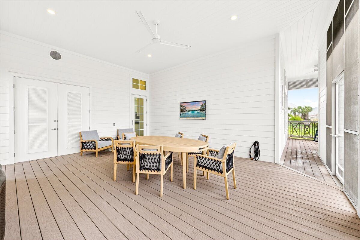 A spacious room with a wooden deck, a round table with chairs, a ceiling fan, and a painting on the wall.