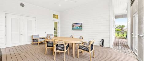 A spacious room with a wooden deck, a round table with chairs, a ceiling fan, and a painting on the wall.
