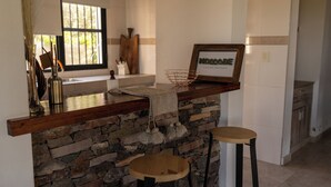 A kitchen with a stone backsplash, wooden counter, two stools, a hanging light fixture, and a framed sign. - Casa Andina: Rustic Warmth, Fire Corner and Total Relaxation in Chacras (Luján de Cuyo)