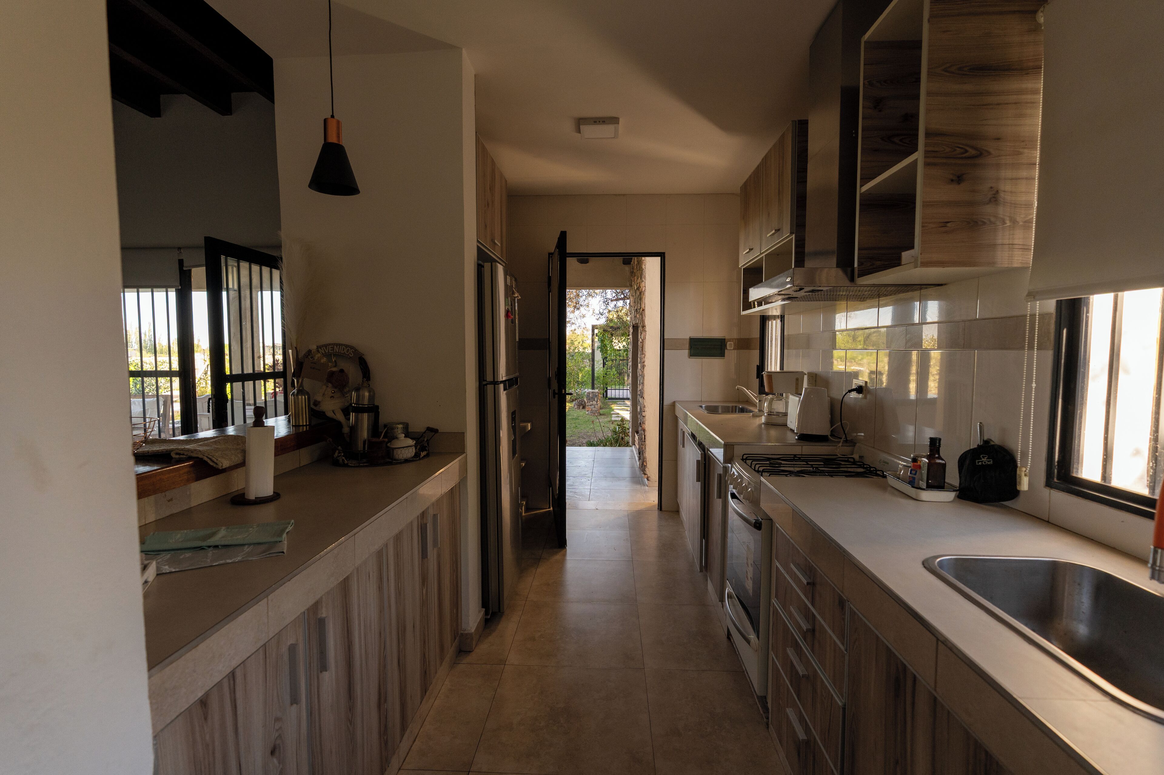 Une cuisine moderne avec des meubles en bois, un évier en acier inoxydable et une vue sur l’extérieur.