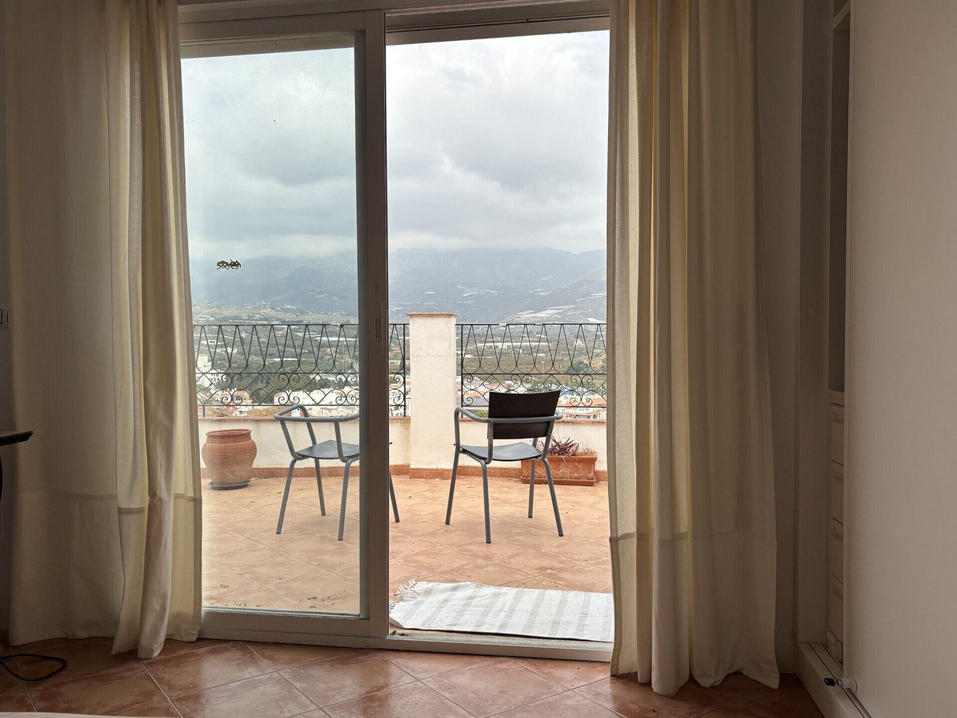 A room with a sliding glass door leading to a balcony with two chairs and a potted plant.