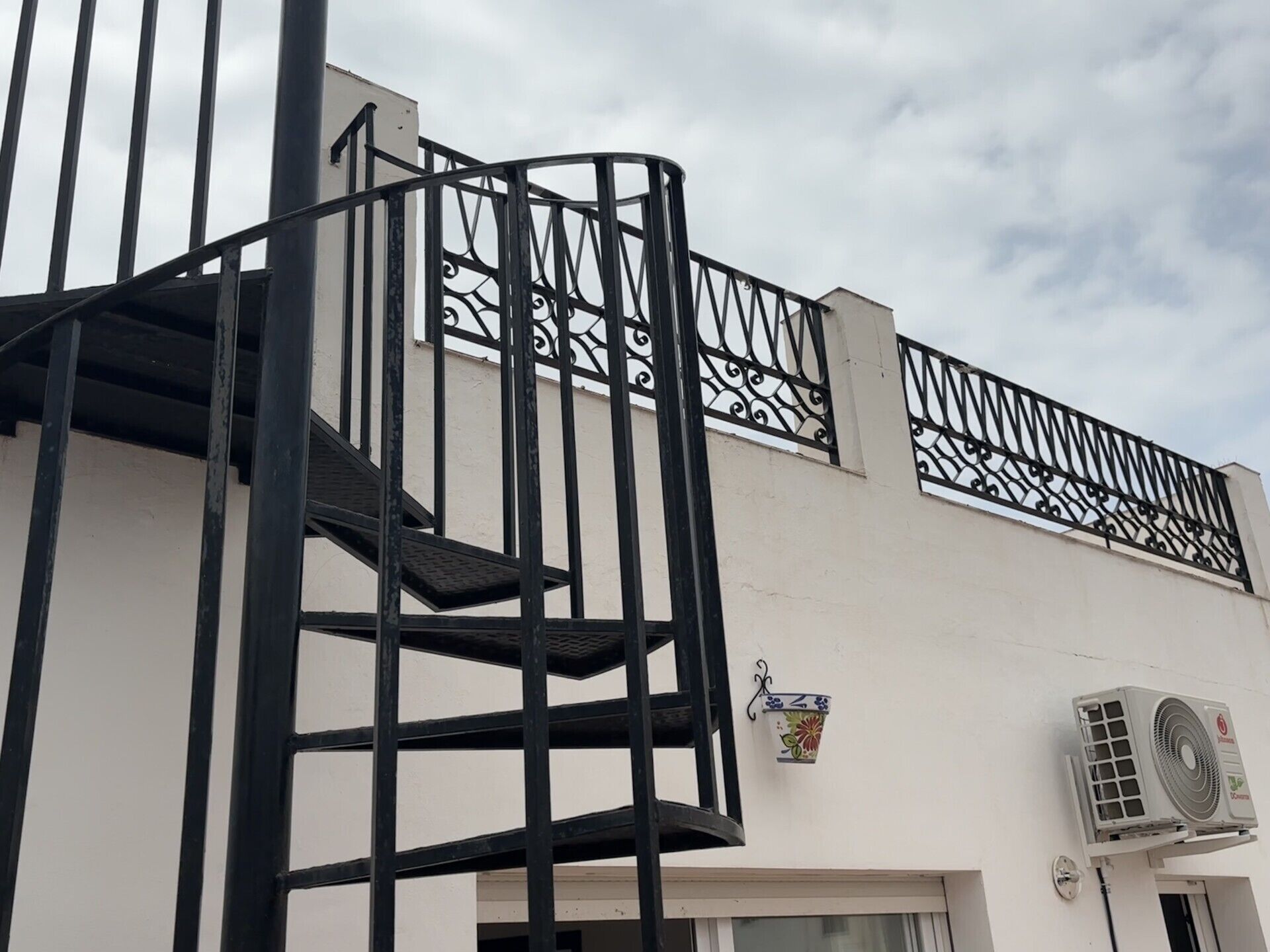 Un edificio con escalera en espiral, unidad de aire acondicionado y una jardinera decorativa montada en la pared.
