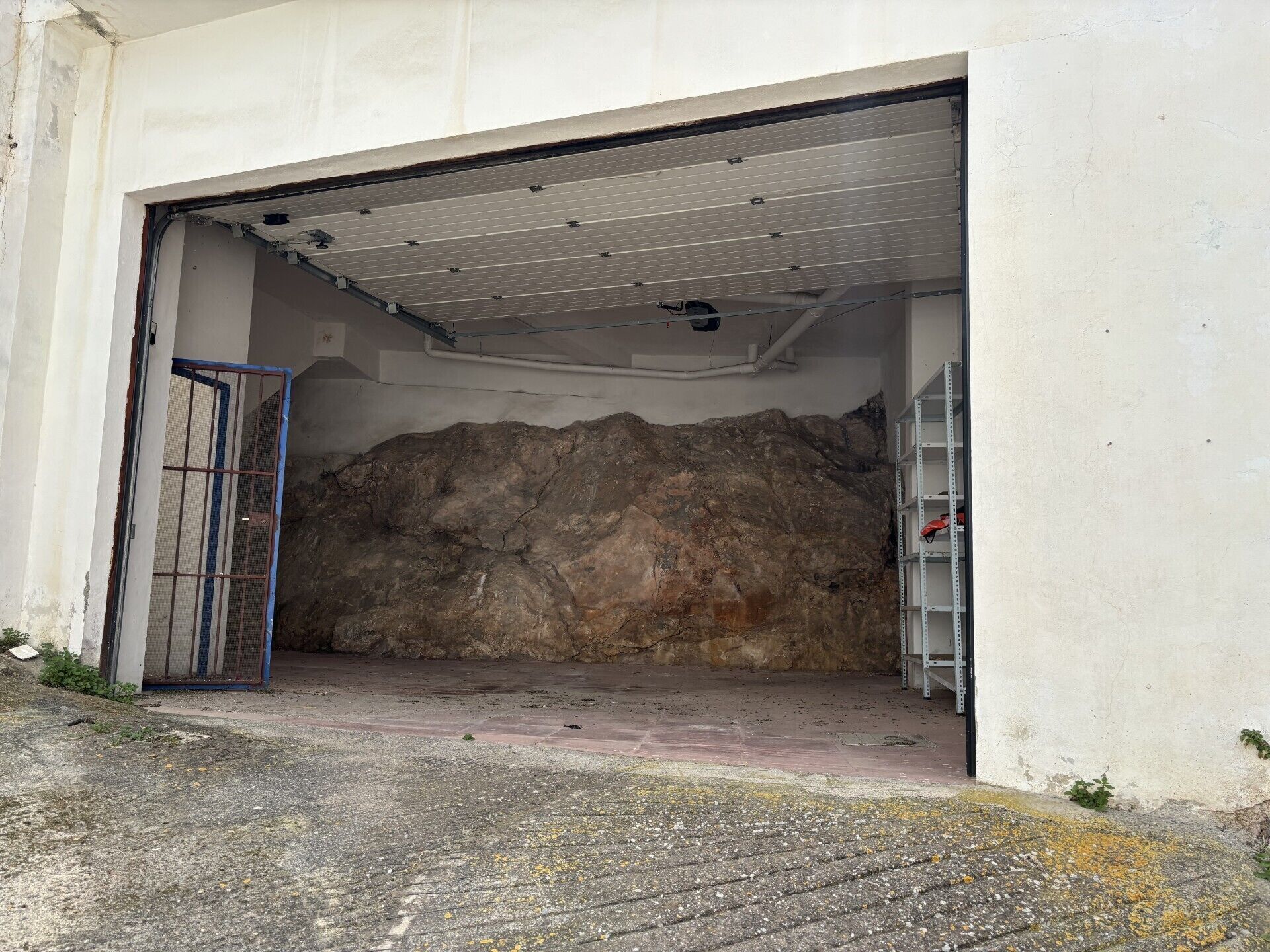 Un garage avec un mur en béton, une porte métallique et une étagère métallique.