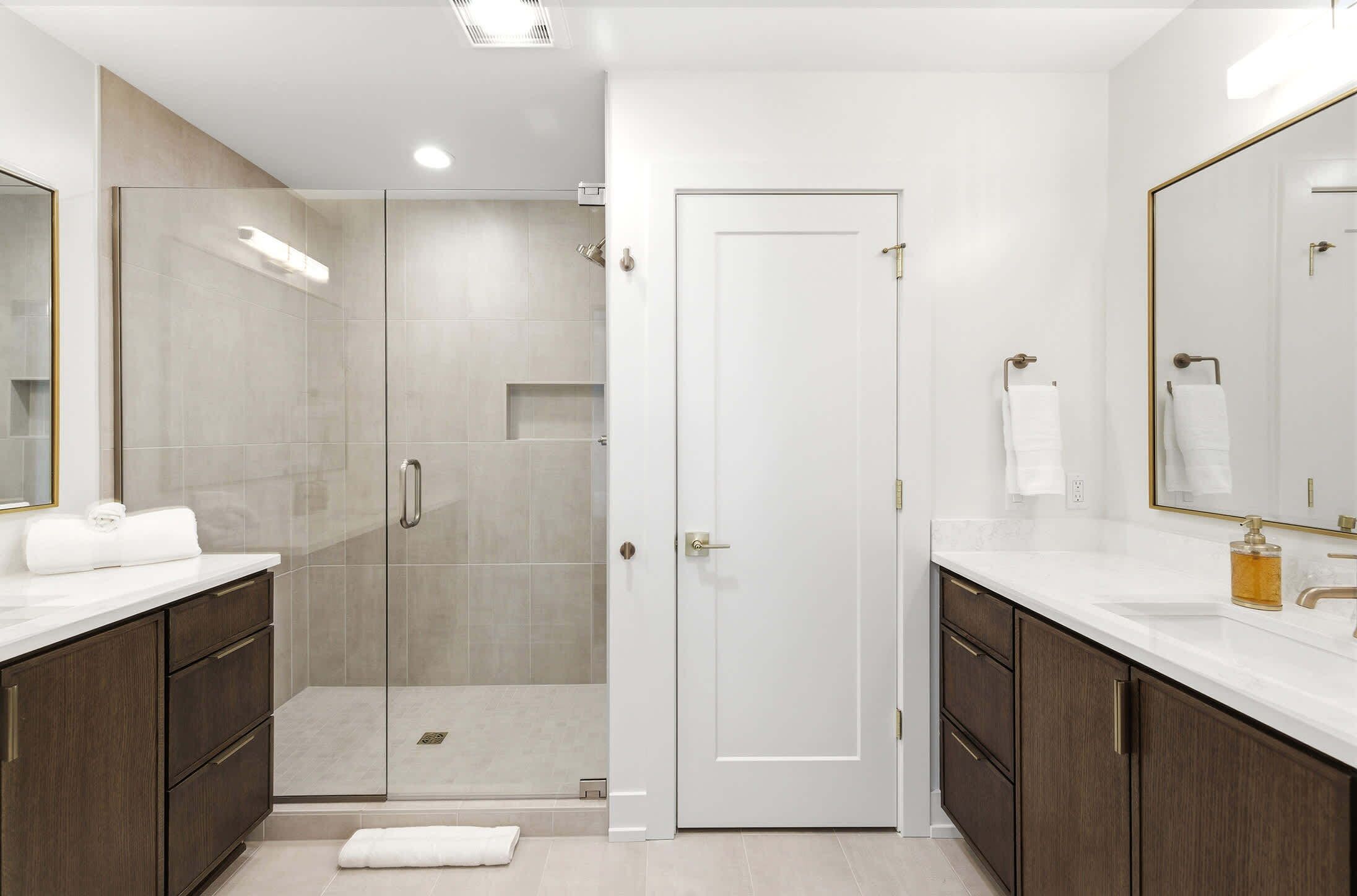 Un baño moderno con ducha acristalada, una puerta blanca y un espejo grande.