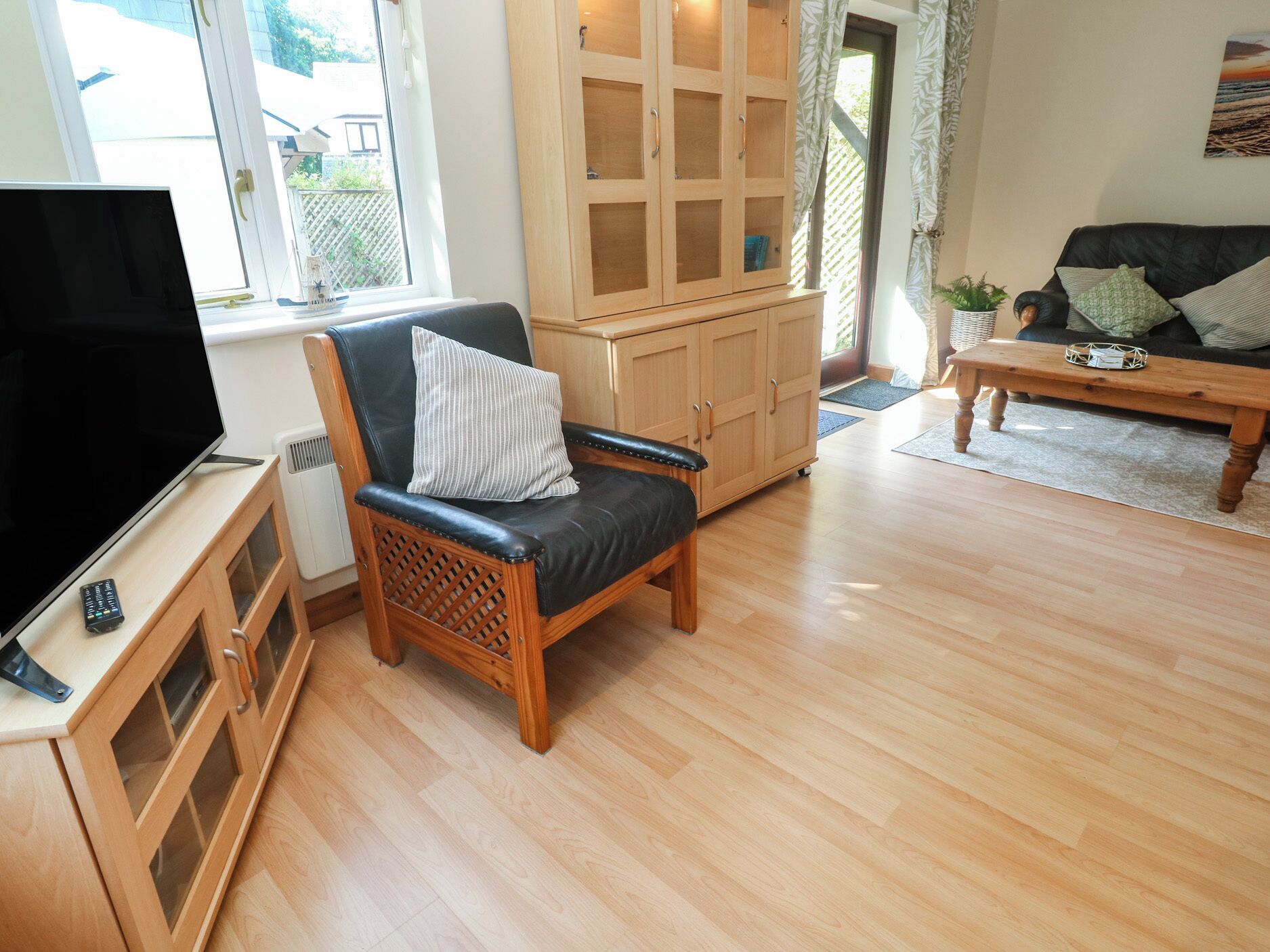 Una sala de estar con un aparador de madera, un sillón de cuero negro, una mesa de centro de madera y un televisor.