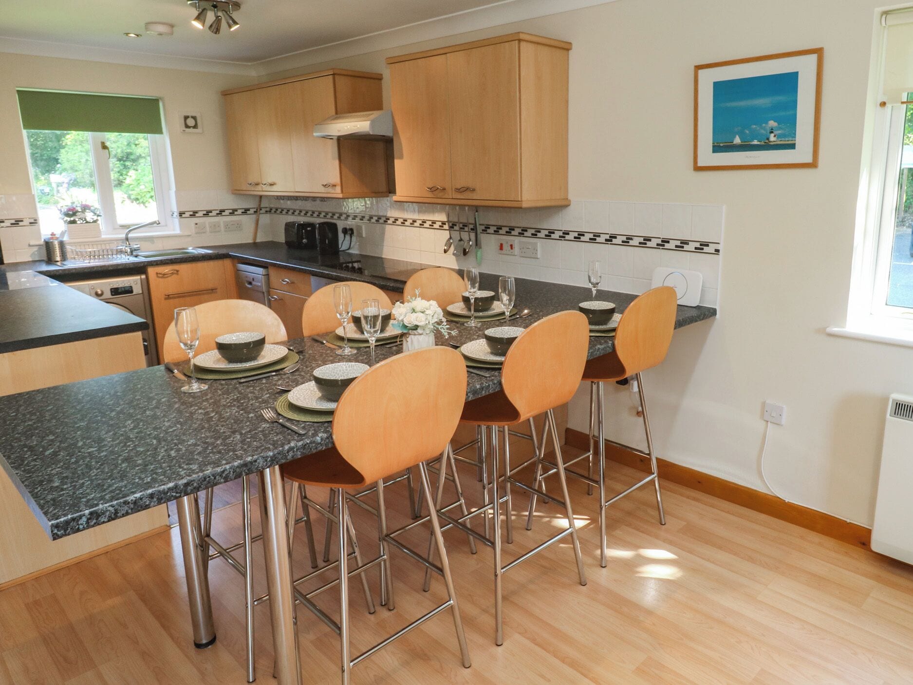Una cocina moderna con armarios de madera, encimera de granito y comedor con cuatro sillas y una mesa dispuesta para dos comensales.