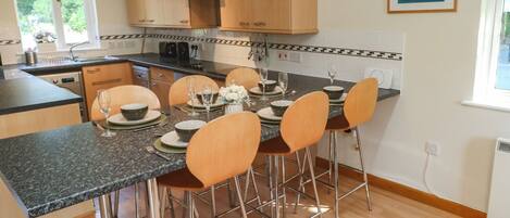 A modern kitchen with wooden cabinets, a granite countertop, and a dining area with four chairs and a table set for two.