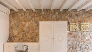 A room with a stone wall, a white wardrobe, a desk with a chair, and decorative wall art. - Casa Tara Retreat  (El Sargento)