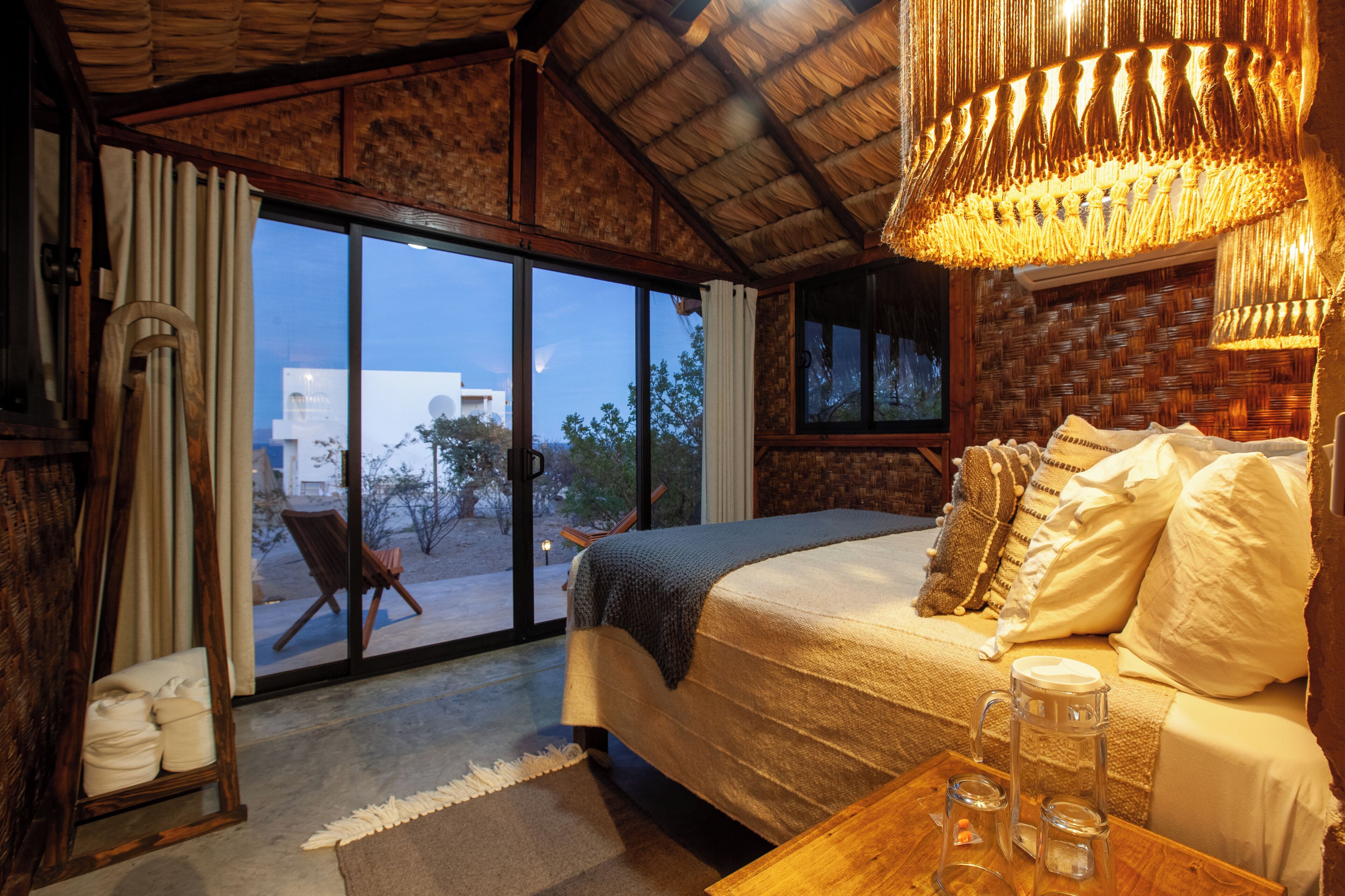 Un dormitorio con una cama grande, un cabecero de madera, una mesa de centro de cristal y vistas a través de la puerta de vidrio.