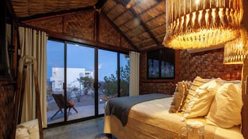 Une chambre avec un grand lit, une tête de lit en bois, une table basse en verre et une vue sur l’extérieur, visible à travers la porte vitrée.