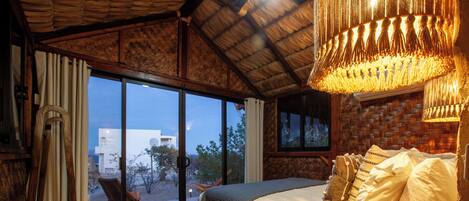 Un dormitorio con una cama grande, un cabecero de madera, una mesa de centro de cristal y vistas a través de la puerta de vidrio.