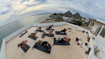 A rooftop yoga class with a view of the sea and a resort building.