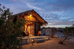 A thatched-roof structure with a seating area and steps leading to the entrance.