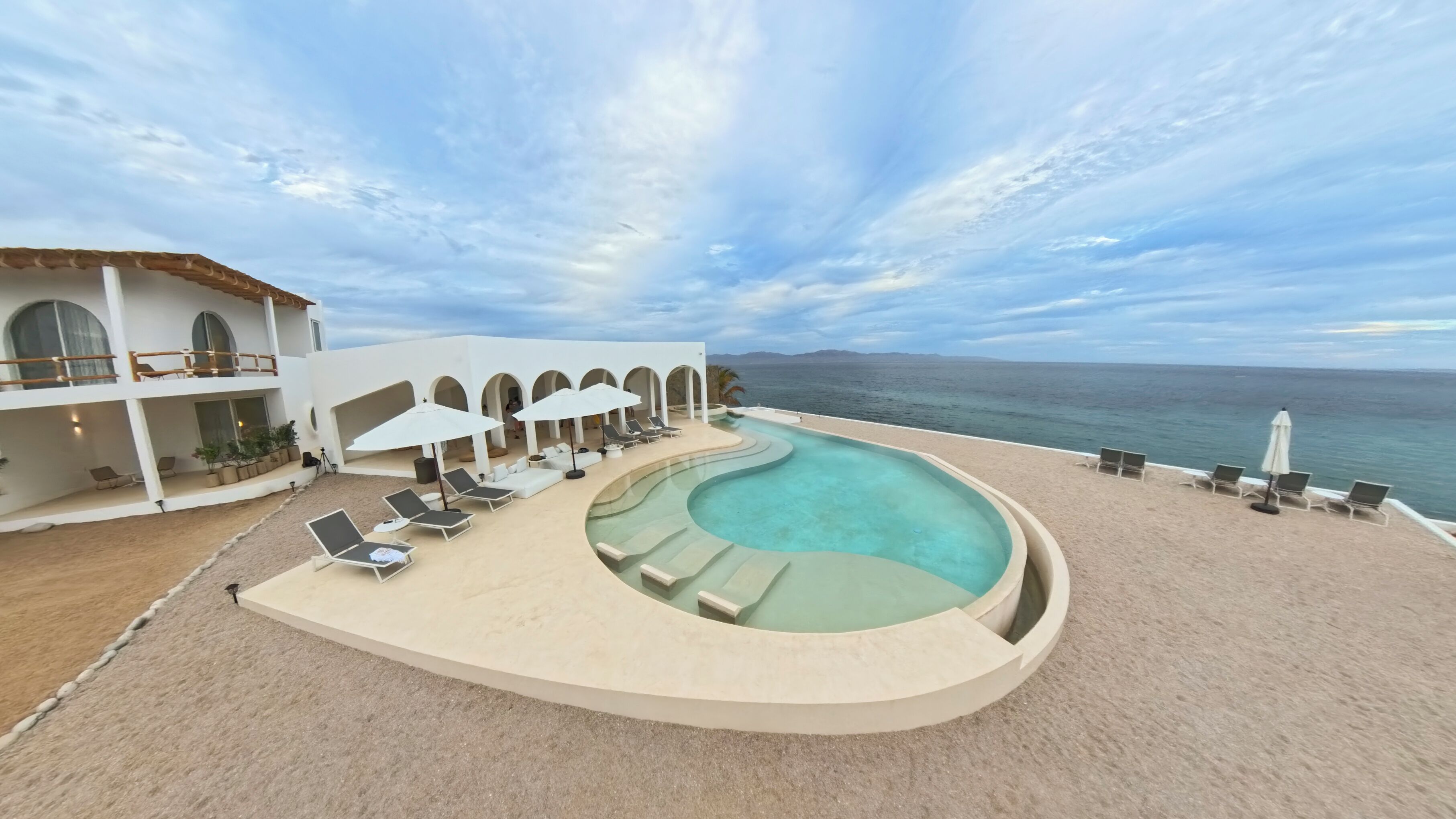 A resort with a pool, lounge chairs, and a view of the ocean.