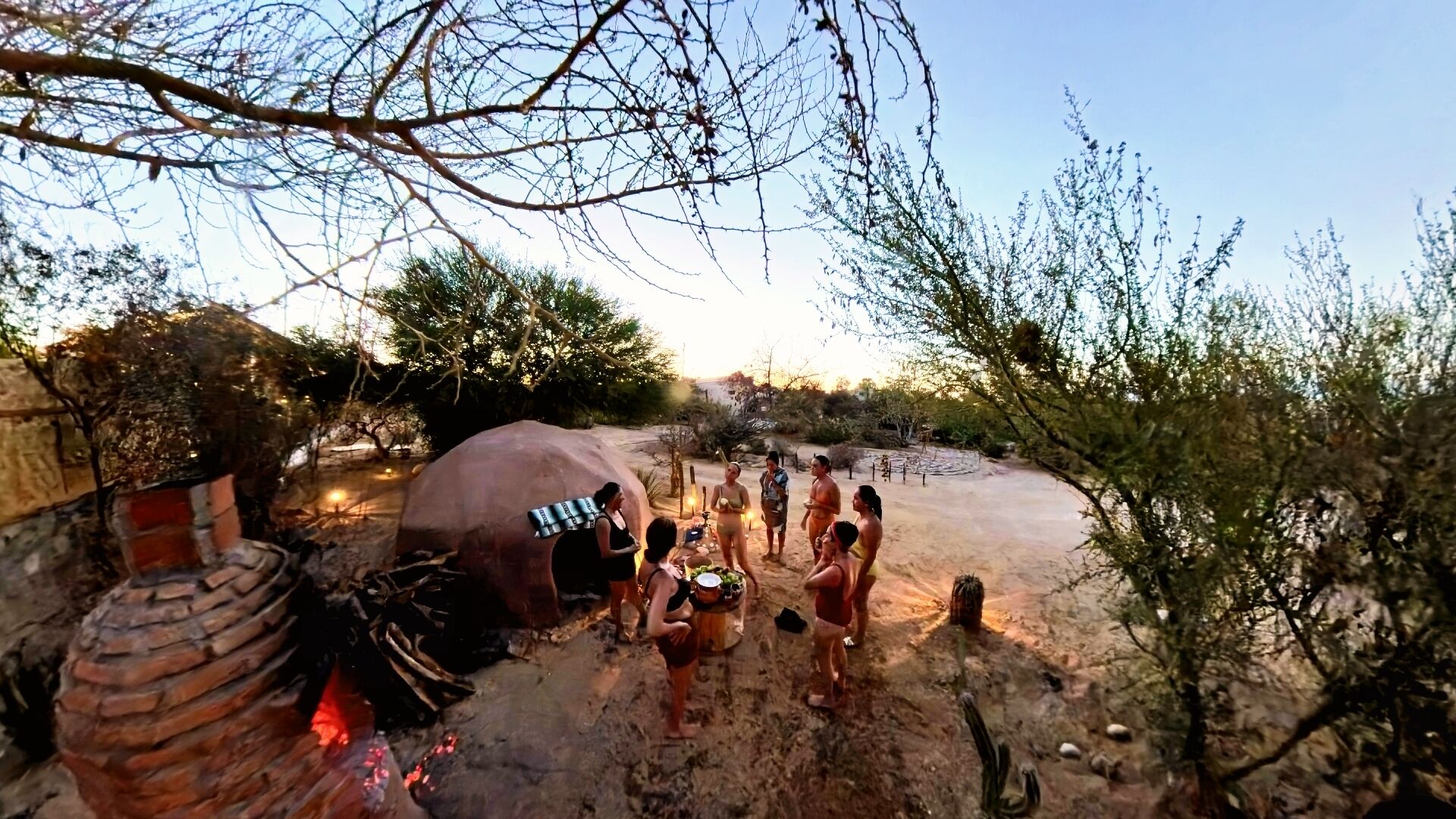 Un grupo de personas alrededor de una fogata en un paisaje desértico con vegetación escasa.