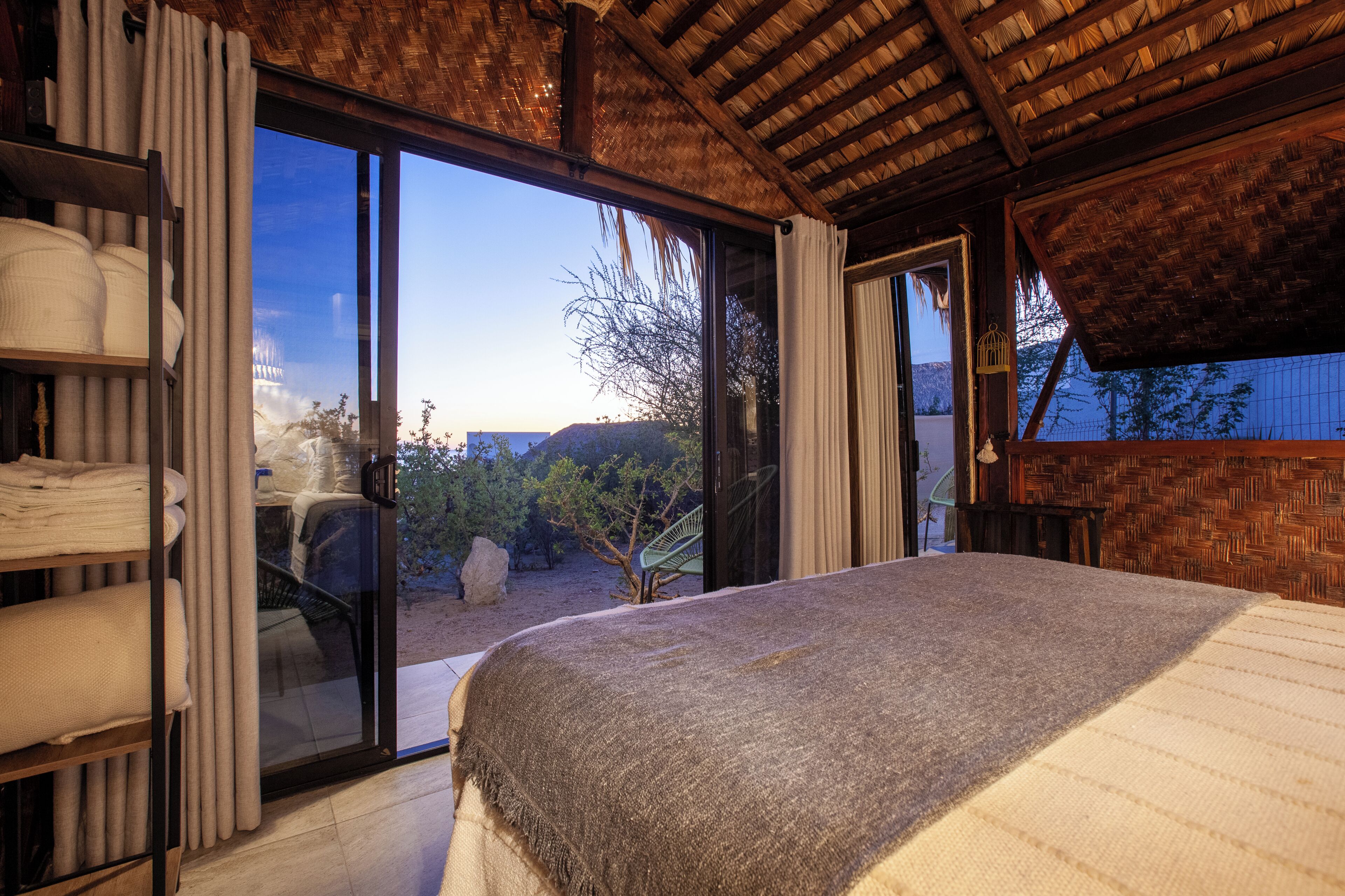 A bedroom with a large bed, a sliding glass door leading to a balcony, and a view of the outdoors.