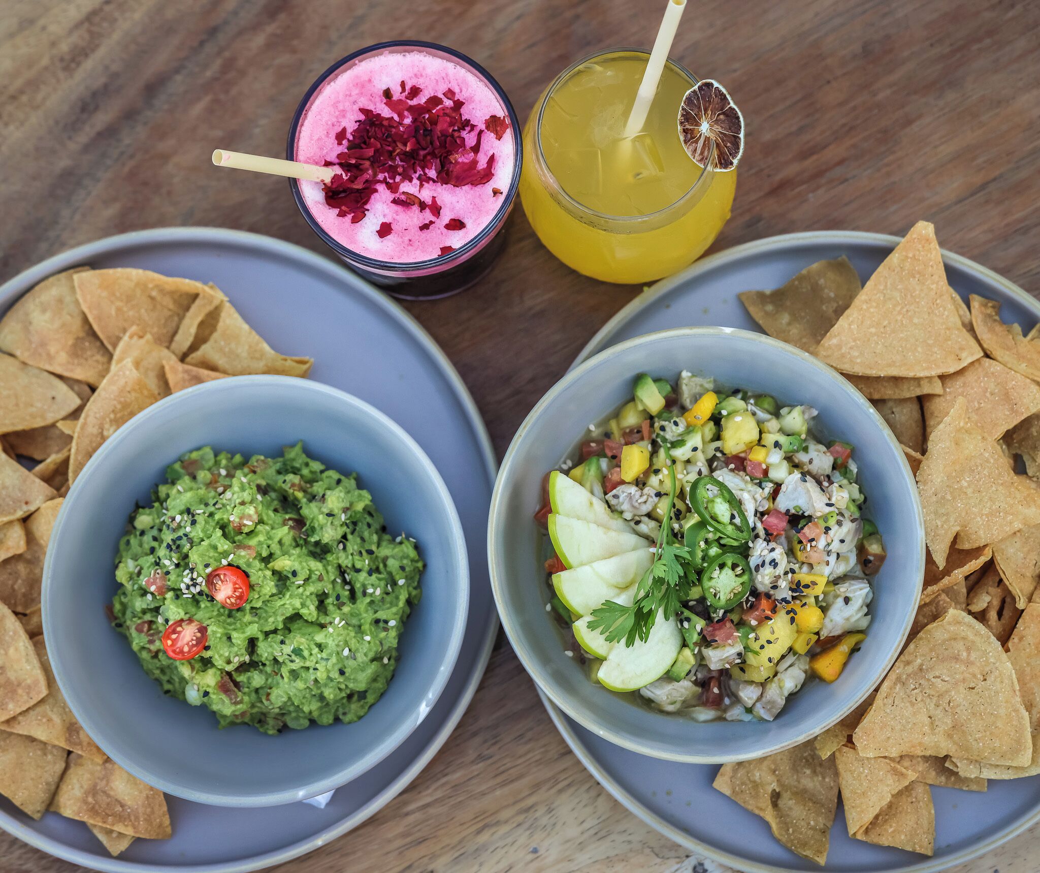 Two bowls of food, one with guacamole and the other with a fruit salad, and two drinks on a table.