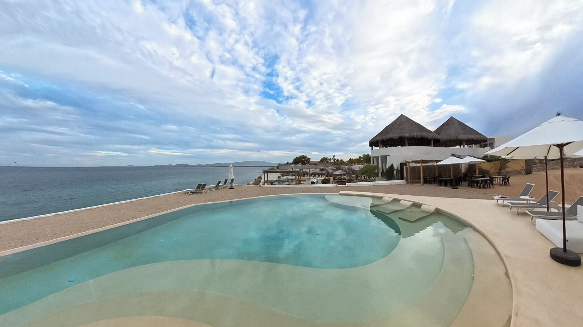 A pool area with lounge chairs, umbrellas, and a view of the sea.