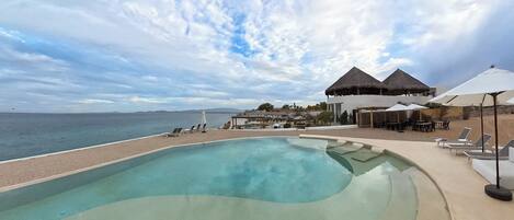 A pool area with lounge chairs, umbrellas, and a view of the sea.