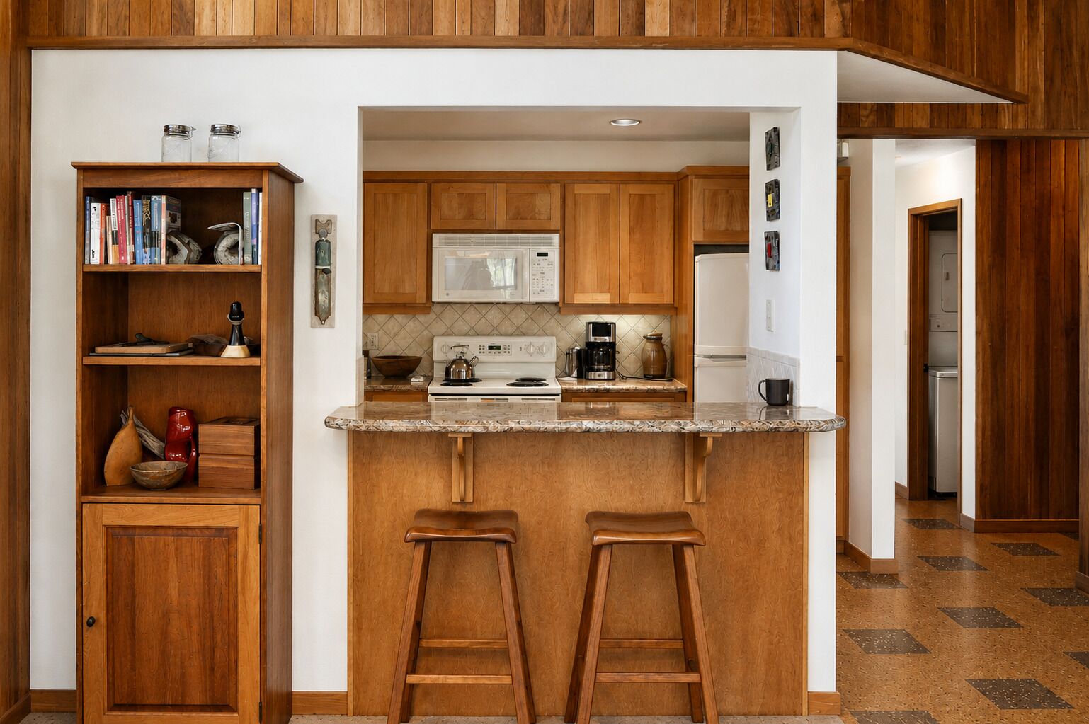A kitchen with wooden cabinets, a granite countertop, a microwave, a stove, and two bar stools.