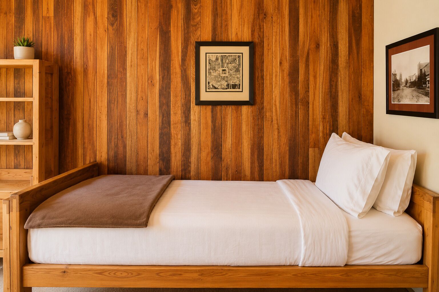 Una cama de madera con ropa de cama blanca, un cuadro enmarcado en la pared y una estantería con una planta y un florero.