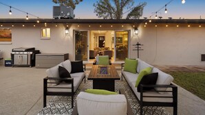 Un espacio al aire libre con patio, sillones, una mesa y luces colgantes.