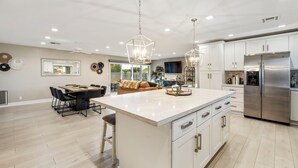 Una cocina amplia con una isla central, armarios blancos y electrodomésticos de acero inoxidable.
