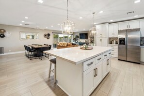 Een moderne keuken met een centraal eiland, roestvrijstalen apparatuur en hangende lampen.