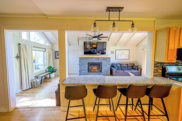 A modern kitchen with a central island, bar stools, a fireplace, and a ceiling fan.