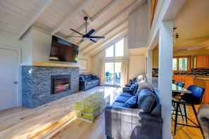 A spacious living room with a fireplace, a ceiling fan, and a large window.