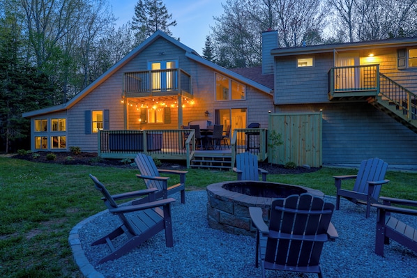 A two-story house with a deck, outdoor seating, and a fire pit.