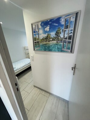 Ein Zimmer mit einem Bett, einer Tür und einer Wandmalerei mit einer tropischen Strandansicht.