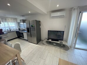Eine moderne Küche mit Edelstahlgeräten, einem Essbereich mit Holztisch und einem Flachbildfernseher auf einem Standfuß.