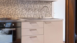 Cuina moderna amb armaris blancs, un frontissis de rajola, un rentamiques d'acer inoxidable i un forn encastrat.