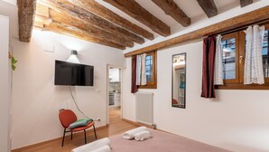 Un dormitori amb sostre de fusta, televisió de pantalla plana, una cadira vermella, un llit amb tovalloles blanques i una finestra amb cortines.